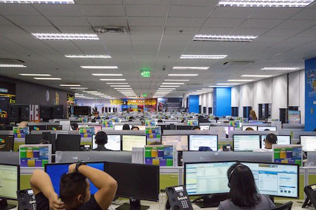 Photo of VXI employees engaged in customer service tasks within a call center environment.