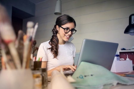 A woman with glasses is working on a laptop at a tech startup.