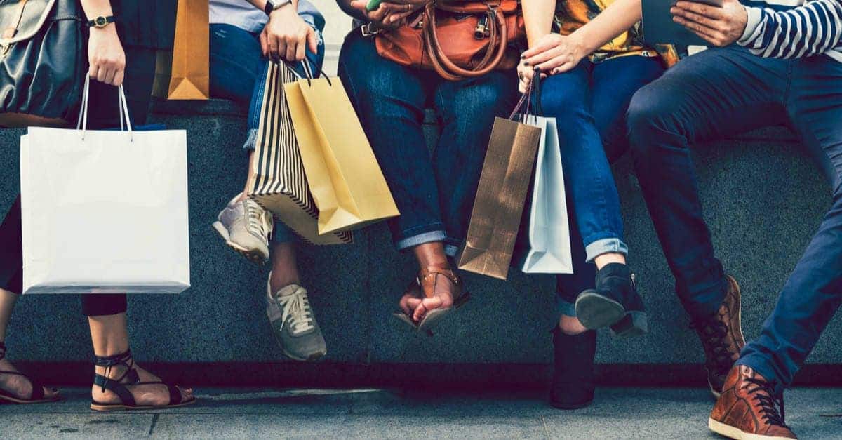 Photo showing a close-up of the lower body of a group of people sitting, surrounded by shopping bags.