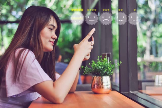 Image displaying a close-up of a woman on her phone while sitting in a restaurant, with a graphic overlay depicting a customer satisfaction survey.