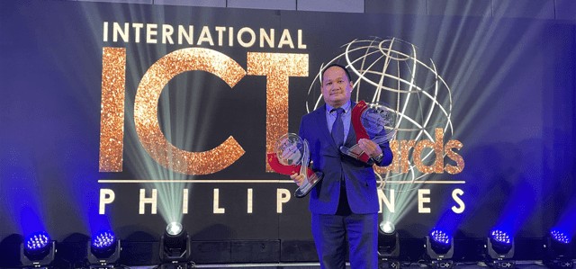 Photo of Eppie Titong, VXI's SVP & Country Manager for the Philippines, holding two awards on stage at the International ICT Awards Philippines ceremony.