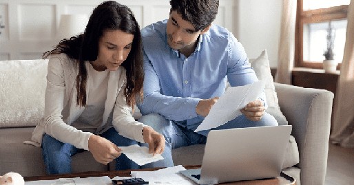 Image of a man and woman sitting on a sofa, leaning over a desk covered with documents, engaged in a discussion.